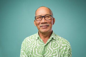 Portrait of Asian senior adult man in green T-shirt and eyeglasses smiling looking at camera...