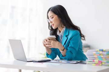 Portrait of Asian business woman holding coffee cup with work in workplace office Business documents money financial planning concept
