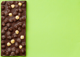 Chocolate with hazelnuts on a green background top view copy space.