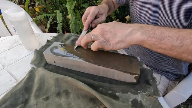 Closeup of a man sharpening his knife on the sharpening stone