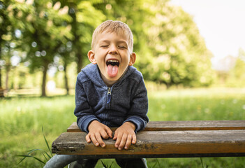 Portrait of silly little blond boy in blue sweater smiling and showing tongue to camera, making funny faces.