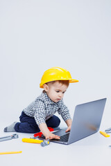 A handsome little boy 2-3 years old in a shirt on a white background is looking at a laptop. A child is playing with a portable laptop