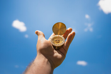 selective focus, hand holding a compass with a blue sky with clouds in the background.travel concept