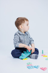 A cute little boy in a checkered shirt sits on a white background and plays with wooden educational toys. Ecological wooden toys for children