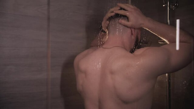 Athletic man takes a shower. Naked back of a young guy.