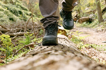 Traveler man has hiking in mountain forest. Close up of human foots in mountain shoe walking on tree log. Exercise and fitness in nature for wellness and healthy lifestyle.