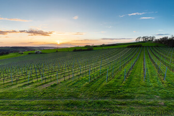 Fototapeta na wymiar Magical sunset with a dramatic cloudscape in the rolling hills and the vineyards of Fromberg, Voerendaal in the South Limburg in the Netherlands during early spring season with amazing sunbeams.