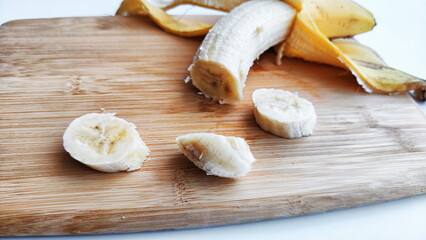 Banana with open panel and sliced round pieces on wooden board and white background. Ripe banana with peel Close up and cooking. Delicious sweet fruit dessert