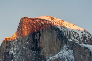 The last light of the setting sun illuminating a snow-covered half-dome on a winter afternoon....