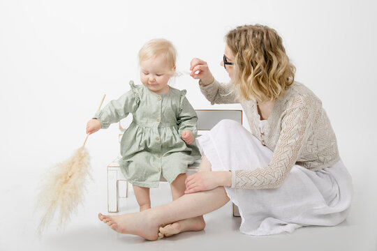 Portrait of cute little blond girl holding branch of dried pampas grass. Young woman tickling face with twig. Family.