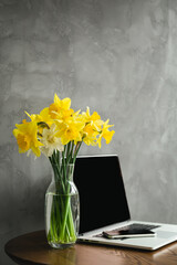 Yellow Daffodils and Laptop on a Desk, textured Grey background, copy space.