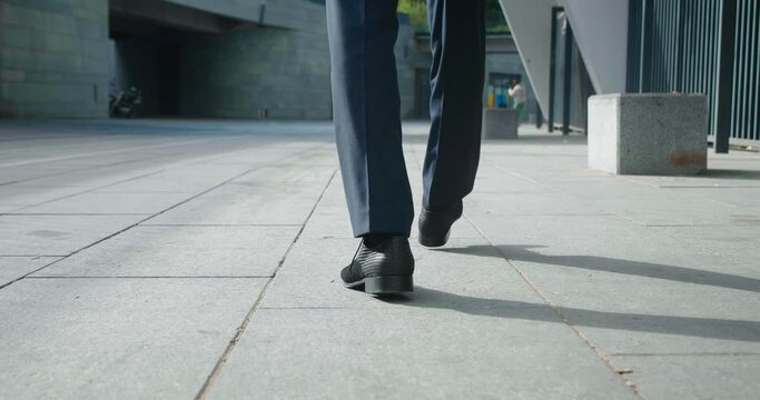 Rear view feet of businessman going to work. Back view of confident man businessman in leather shoes and formal suit walking downtown near office building. Close up feet of businessman at city outdoor