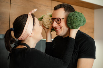 Portrait of loving family cooking together in kitchen. Wife holding green cauliflower at husbands head instead of ears.