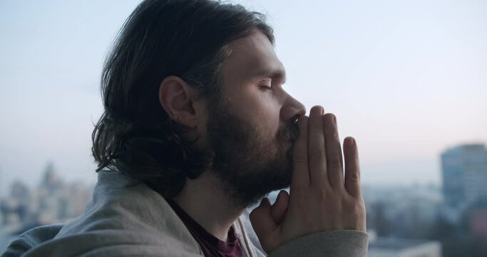 Man is praying to God with closed eyes and hands together, asking for help with problems and expressing gratitude for all he have. Faith, hope, and Christian beliefs concept