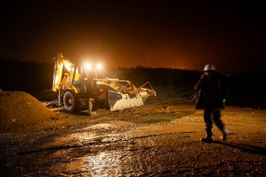 Ust-Luga, Leningrad oblast, Russia - November 16, 2021: Road construction site at night. Excavator and work. Worker right, blurred