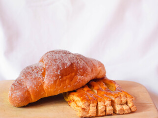 Dos panes dulces, uno sobre otro en fondo blanco sobre una tabla de madera, un cuernito o croissant con azúcar y un pan de miel