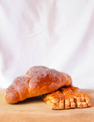 Dos panes dulces, uno sobre otro en fondo blanco sobre una tabla de madera, un cuernito o croissant con azúcar y un pan de miel