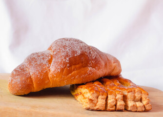 Dos panes dulces, uno sobre otro en fondo blanco sobre una tabla de madera, un cuernito o croissant...