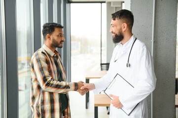 medicine, healthcare and people concept - happy doctor with clipboard and young male patient...