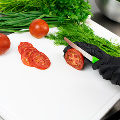 Hands of cook in black rubber gloves cuts tomatoes
