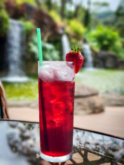 A red tropical drink in a tall glass with ice and a straw