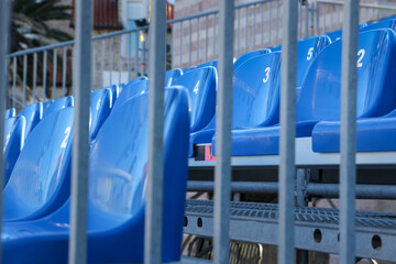 View on rows of blue empty seats in a row through the vertical metal bars.