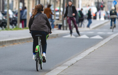 Une femme en train d'écouter de la musique à vélo avec un casque.  - obrazy, fototapety, plakaty