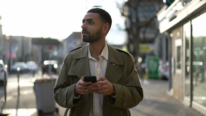 One Arab young man searching for location while walking in city street and holding cellphone. A...