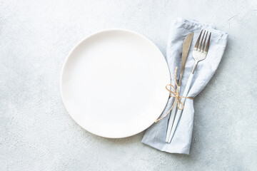 White plate and cutlery on stone table. Empty plate top view.