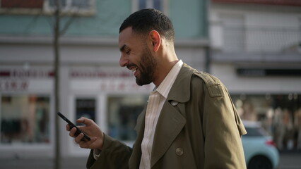 One Happy Middle Eastern man walking in city street holding phone laughing and smiling. A joyful...