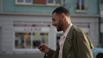 One Happy Middle Eastern man walking in city street holding phone laughing and smiling. A joyful...