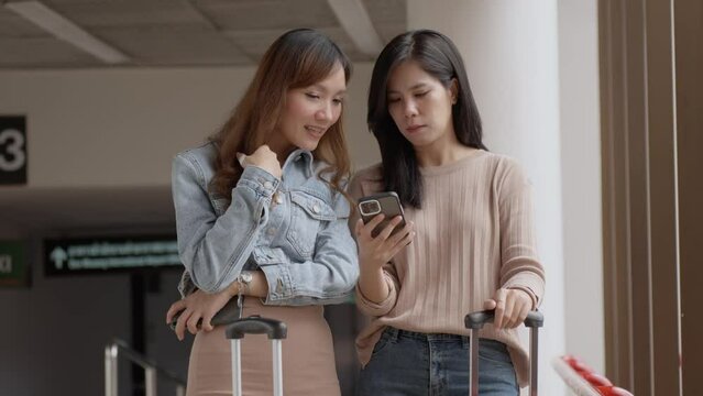 Young adult asian women traveller talking together and using smartphone for checking boarding time at airport. Lifestyle and travel concept.