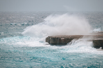 The waves hit the rocks with great splashes. Rocky seashore with blue water, big waves