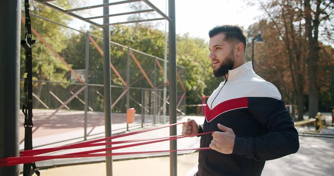 Attractive fitness man does exercising outside. Trainer male correcting fit does gym exercises with rubber band . Outdoor Athletic man does exercises with elastic band. Gym health outside concept.