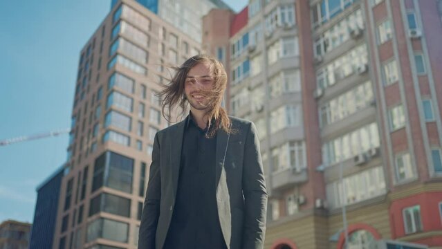 Portrait handsome man in coat looking at camera stand outdoors on background stairs. Sunlight at city street. Slow motion