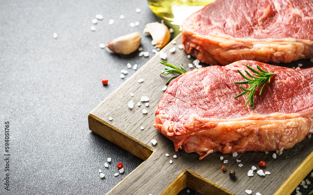 Wall mural Raw Beef steaks with spices. Raw beef meat at cutting board. Close up.