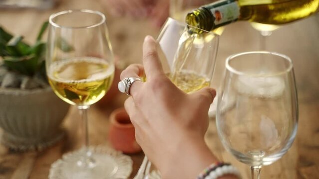 Woman fill glasses of her friends pouring white wine in sea view restaurant. Female hands hold bottle of alcohol drink celebrating birthday, New Year, hen party in bar close-up. Girls night out.