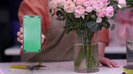 bouquet of flowers on the table and florist woman hand holding smartphone with green screen mock up for flower delivery. ordering flowers online