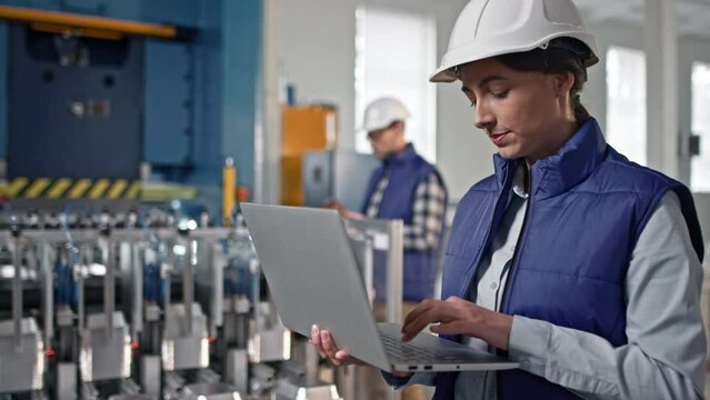 Close-up portrait of beautiful middle-aged female engineer looking watching at product making process. Woman nodding and putting information into her big grey gadget.