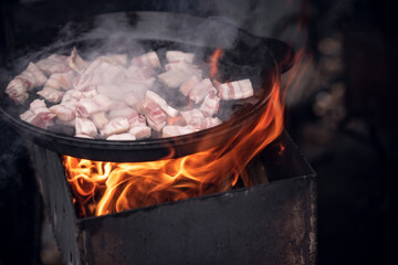Cooking food at a picnic. Roasting meat and bacon in a large metal frying pan.