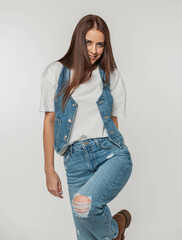 Stylish beautiful young woman model with a smile in fashionable jeans clothes with a denim vest, T-shirt and jeans poses and having fun on a white background in the studio