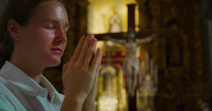 Christian woman prays on her knees in church against the background of crucified Jesus Christ. Close-up religious girl face in temple worshiping God.