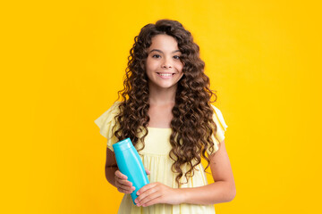 Teenager child girl showing bottle shampoo conditioners or shower gel isolated on yellow background. Hair cosmetic product. Mock up bottle. Happy teenager portrait. Smiling girl.