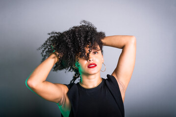 Beautiful young woman standing against gray background messing with her black hair.