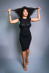 Beautiful young woman standing against gray background messing with her black hair.