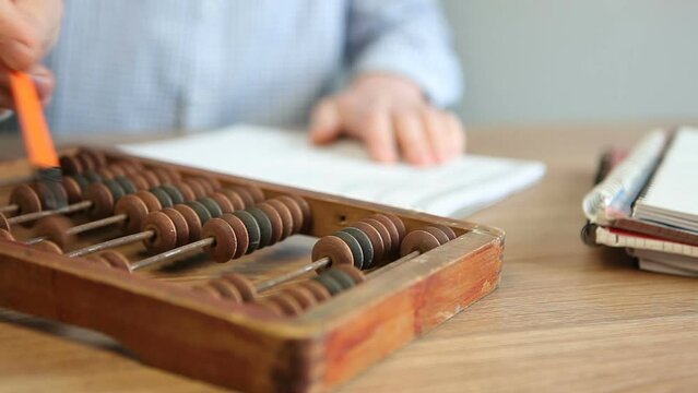 A male accountant counts on wooden abacus while sitting at a table in the office. Counting board with bones to perform arithmetic calculations.