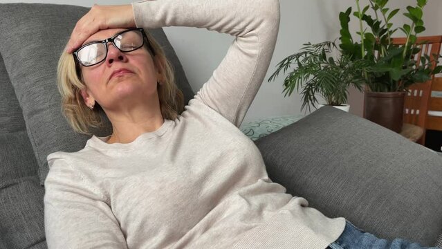 A middle-aged woman lies on the couch with a headache, a migraine. The concept of menopause, hormonal changes. Abnormal heat