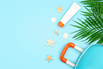 Suitcase, sunscreen tube, seashells and palm leaves on blue background. Summer holidays concept. Top view with copy space