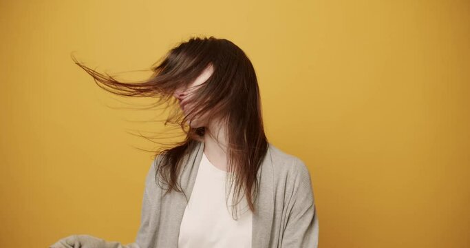 Happy young brunette dancing energetically. Merry young woman in stylish clothes shaking long dark hair and smiling gleefully while performing energetic dance against yellow background