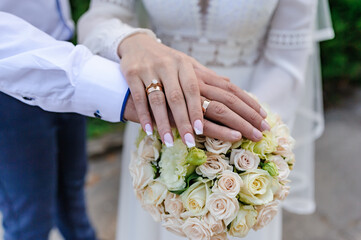 Obraz na płótnie Canvas Wedding gold rings on the hands of the newlyweds, a bouquet of flowers in the background. Gold rings on the hand of a man and a woman